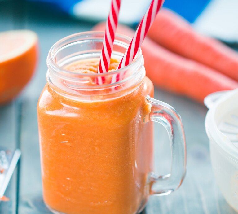 Ein Glas mit dem Karotten-Orangen-Smoothie auf einem dunkelblauen Tisch. | © Shutterstock/ yari2000