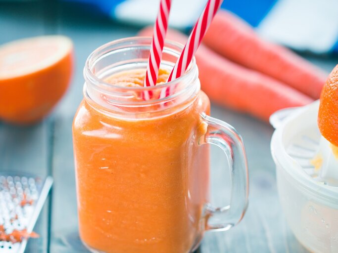 Ein Glas mit dem Karotten-Orangen-Smoothie auf einem dunkelblauen Tisch. | © Shutterstock/ yari2000