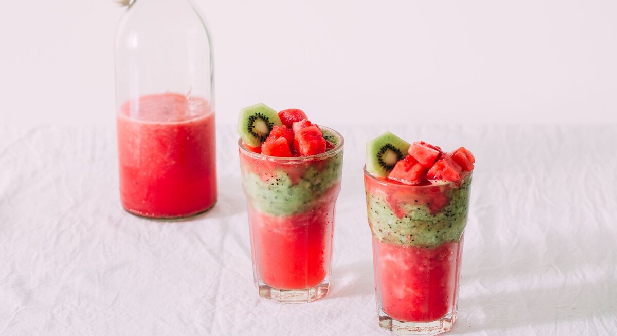 Zwei Gläser mit dem Wassermelonen-Kiwi-Smoothie auf weißem Unter- und Hintergrund.