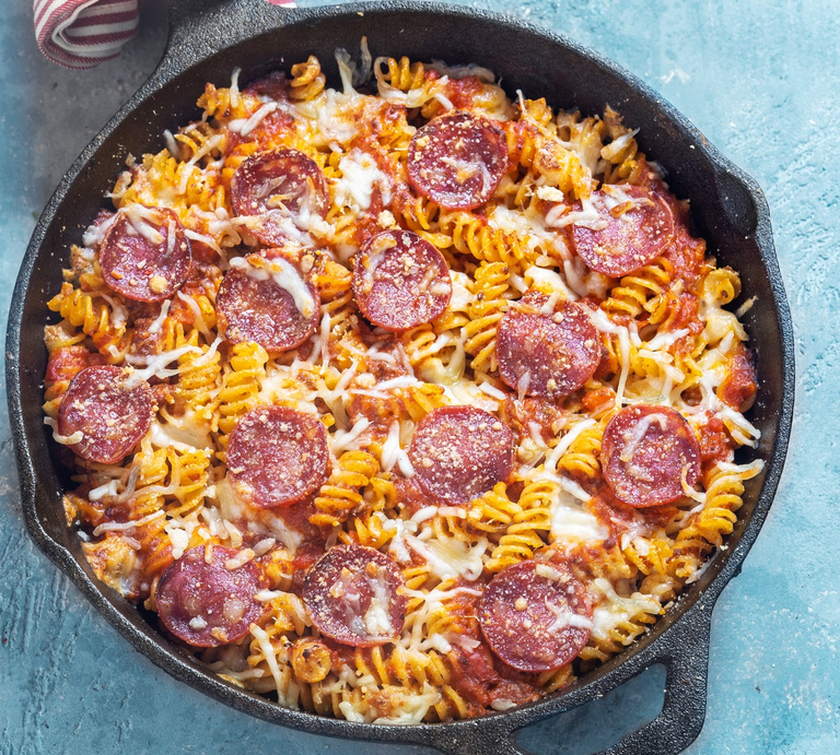 Spirelli-Salami-Pfanne mit Tomaten in Gusspfanne auf blauem Untergrund. Oben im Bild rot-weiß-gestreiftes Tuch. Aufnahme aus der Vogelperspektive. | © Getty Images/Carlo A