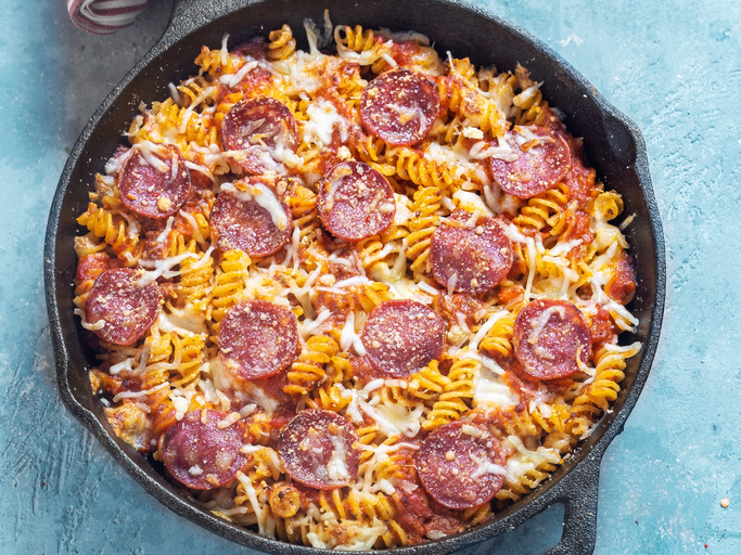Spirelli-Salami-Pfanne mit Tomaten in Gusspfanne auf blauem Untergrund. Oben im Bild rot-weiß-gestreiftes Tuch. Aufnahme aus der Vogelperspektive. | © Getty Images/Carlo A