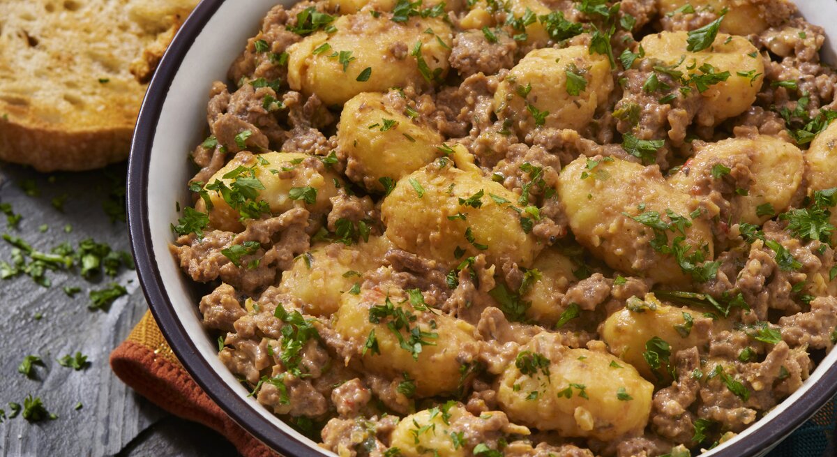 Gnocchi-Pfanne mit Schmand-Hackfleisch auf weißem Teller mit braunem Rand. Das Ganze steht auf einer Schieferplatte.