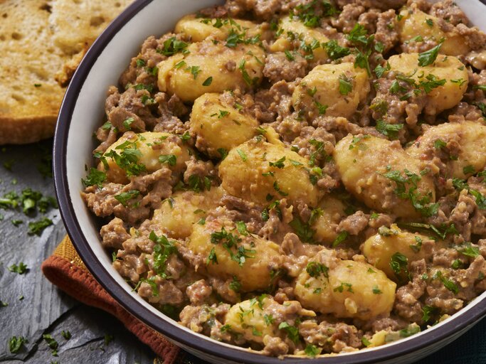 Gnocchi-Pfanne mit Schmand-Hackfleisch auf weißem Teller mit braunem Rand. Das Ganze steht auf einer Schieferplatte. | © Getty Images/ 	LauriPatterson
