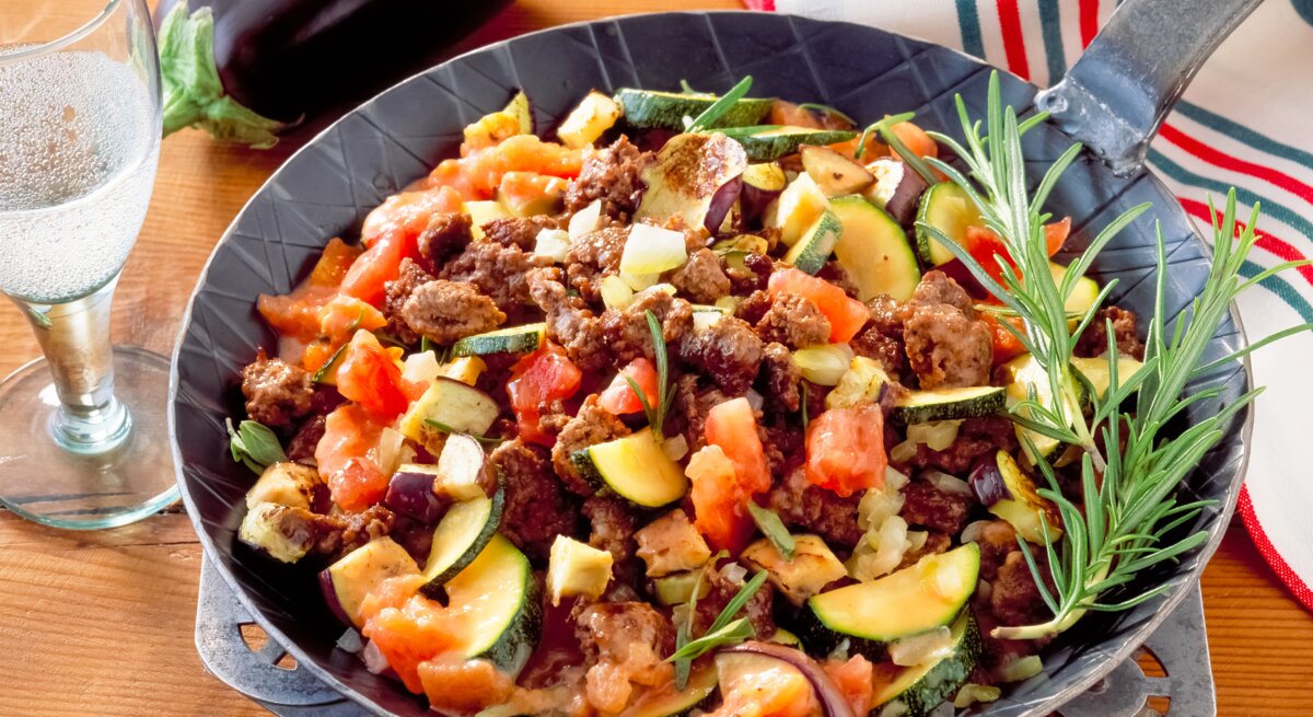 Zucchini-Hackfleisch-Pfanne mit Tomaten auf Holztisch. 