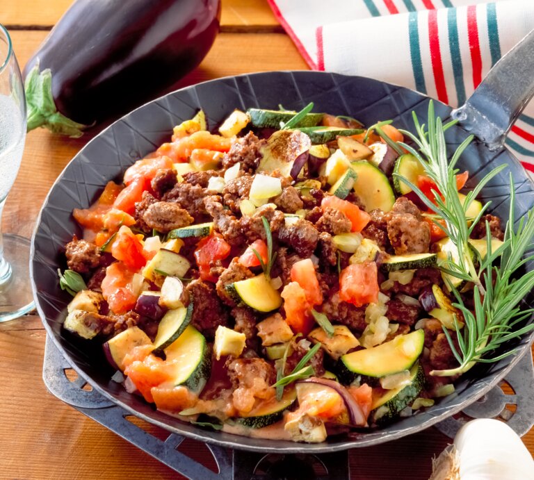 Zucchini-Hackfleisch-Pfanne mit Tomaten auf Holztisch.  | © Shutterstock/Jack Jelly