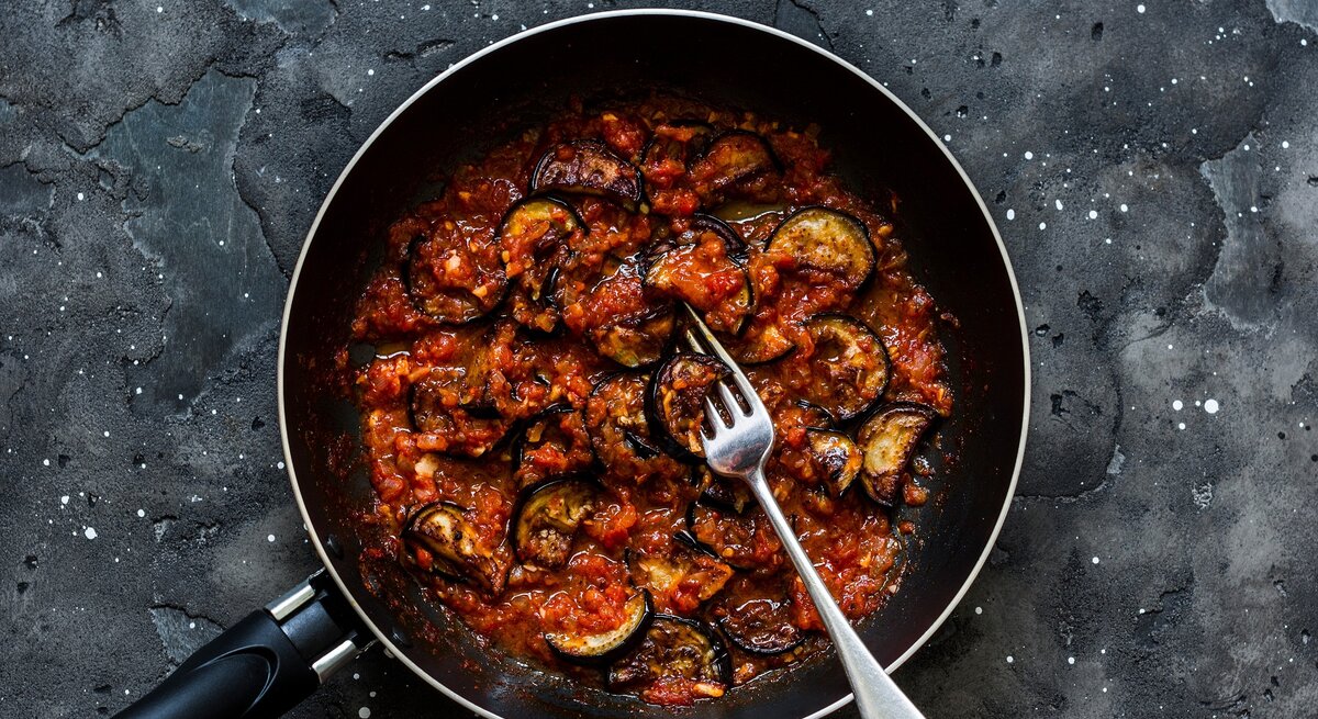 Eine schwarze Pfanne auf dunklem Steinuntergrund mit der Auberginenpfanne.