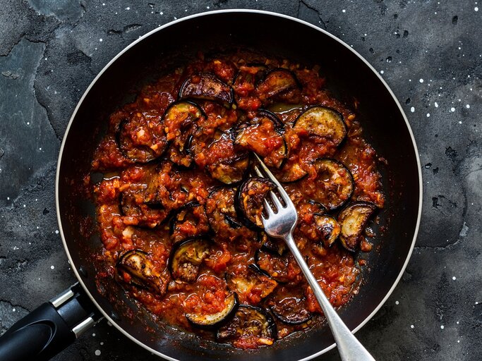 Eine schwarze Pfanne auf dunklem Steinuntergrund mit der Auberginenpfanne. | © Shutterstock/ Kiian Oksana 