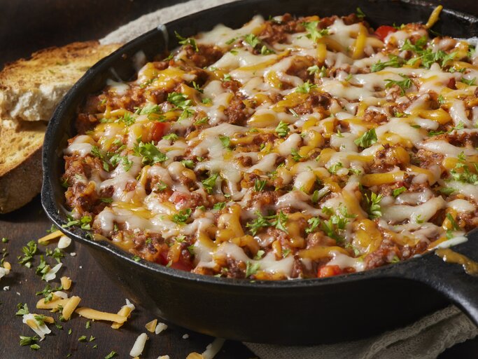Italienische Hackfleisch-Reis-Pfanne mit frischen Kräutern und verlaufenem Käse in einer gusseisernen Pfanne. | © Getty Images/LauriPatterson