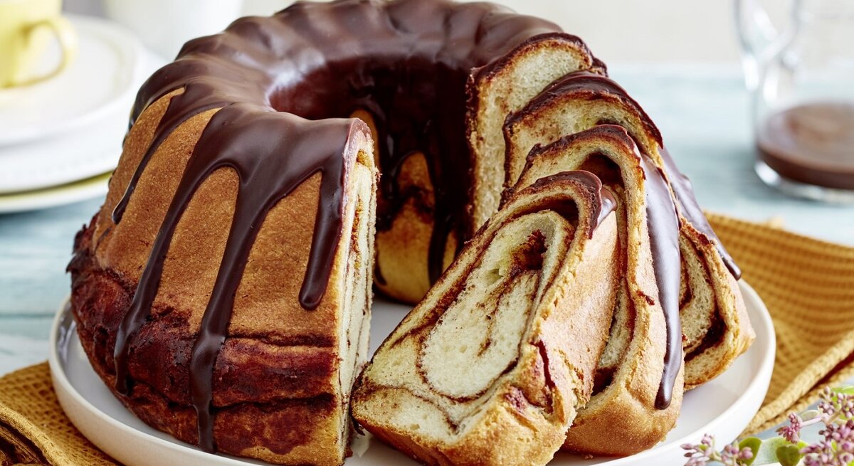 Auf einem Teller steht ein angeschnittener Zimtschnecken-Gugelhupf. Er ist mit einer Schokoladenglasur überzogen. 