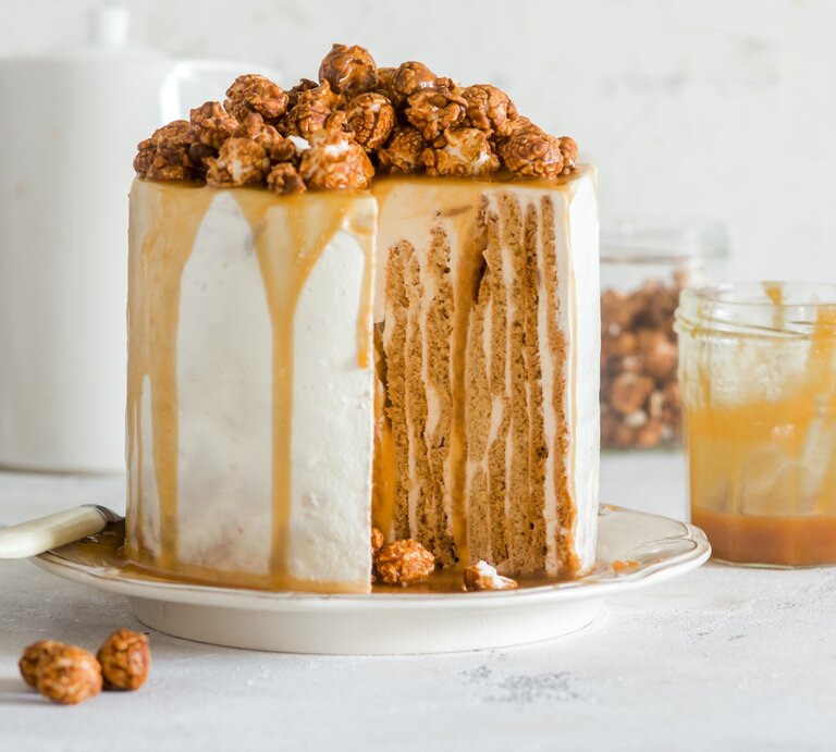 Angeschnittener Nusskuchen mit Karamell und Karamellpopcorn darauf, daneben Glas mit Karamell, heller Hintergrund.  | © Stockfood / Meliukh Irina