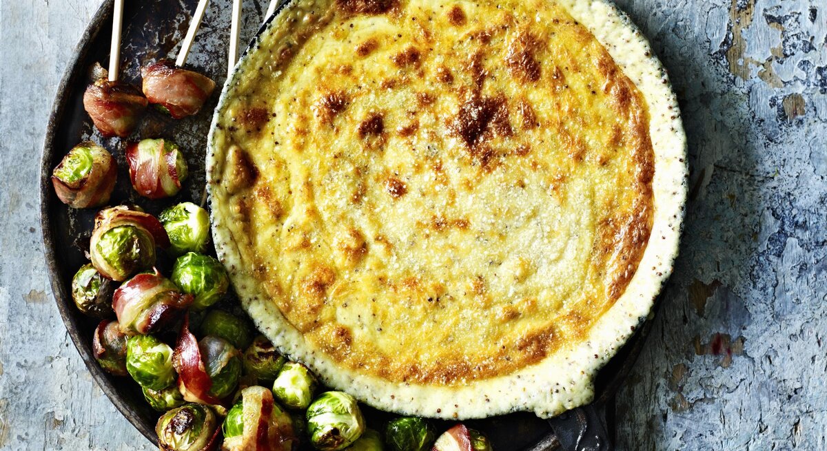 Gebackenes Gruyere-Senf-Fondue mit Rosenkohl im Speckmantel in der Draufsicht.