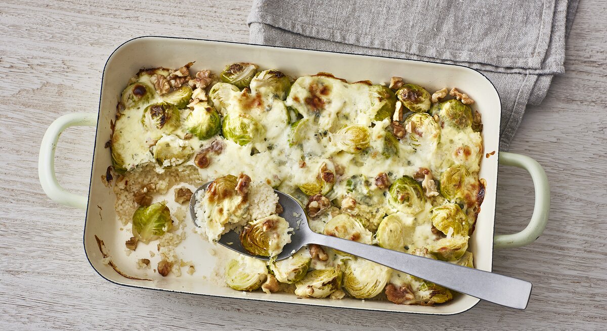 Ofencouscous mit Rosenkohl, Walnüssen und überbackenem Blauschimmelkäse in einer Form auf hellem Untergrund 
