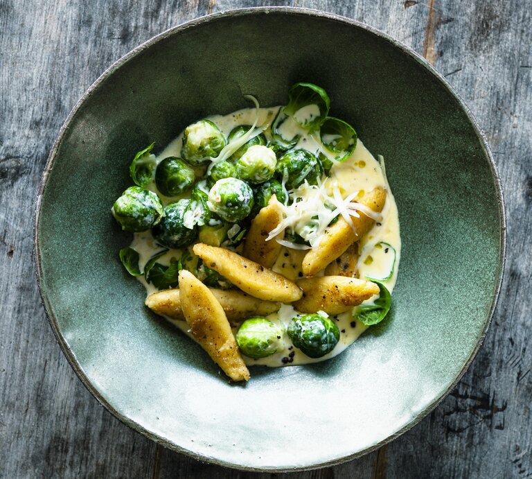 Schupfnudeln und Rosenkohl in heller Soße mit geriebenen Käse. Serviert in mattgrüner Schale auf grauem Holztisch. | © StockFood / Gräfe & Unzer Verlag / Schardt, Wolfgang