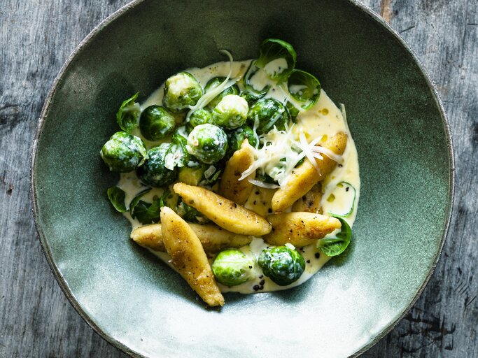 Schupfnudeln und Rosenkohl in heller Soße mit geriebenen Käse. Serviert in mattgrüner Schale auf grauem Holztisch. | © StockFood / Gräfe & Unzer Verlag / Schardt, Wolfgang