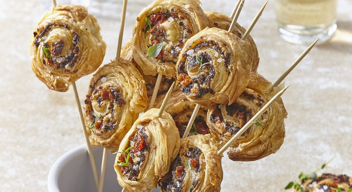 In einem Glas stehen mehrere Blätterteig-Parmesan-Lollies. Sie sind knusprig und goldbraun gebacken. 