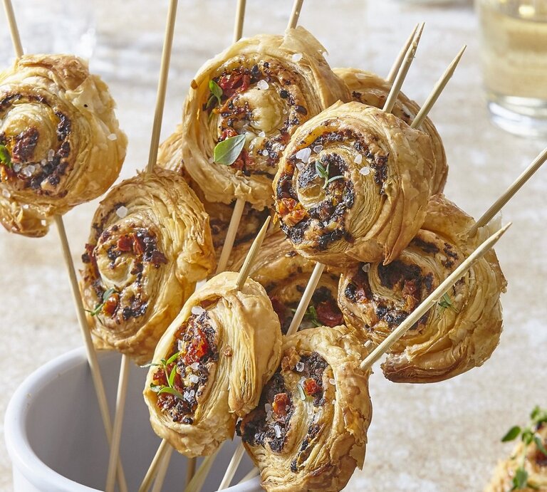 In einem Glas stehen mehrere Blätterteig-Parmesan-Lollies. Sie sind knusprig und goldbraun gebacken.  | © StockFood / Profimedia