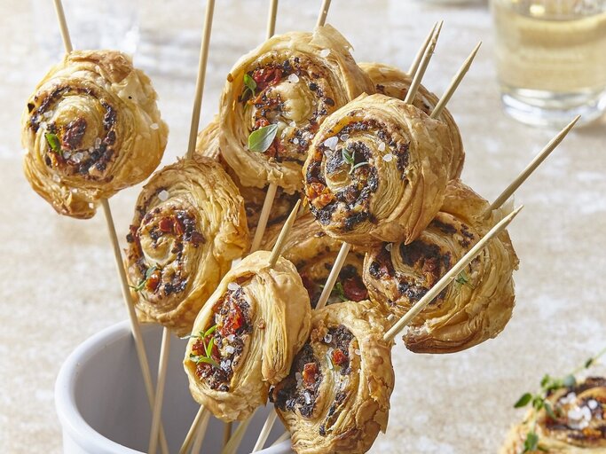 In einem Glas stehen mehrere Blätterteig-Parmesan-Lollies. Sie sind knusprig und goldbraun gebacken.  | © StockFood / Profimedia