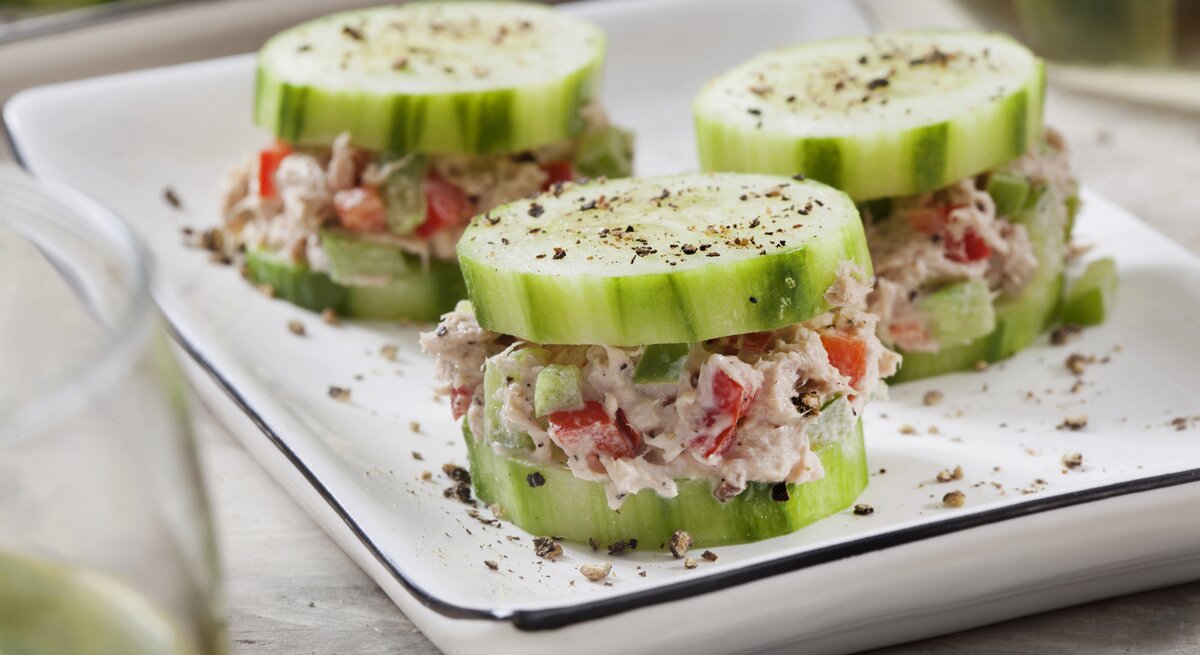 Auf einer weißen Porzellanschale sind drei kleine Gurken-Häppchen mit Thunfisch. Es handelt sich um Fingerfood.
