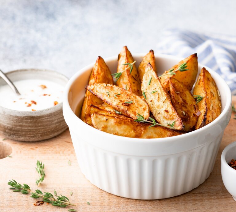 Kohlrabi-Wedges mit Thymian in einer weißen Schale auf einem Brett, darauf außerdem eine Schale Dip und eine Schale mit getrockneten Gewürzen.  | © adobe Stock/ CHZU