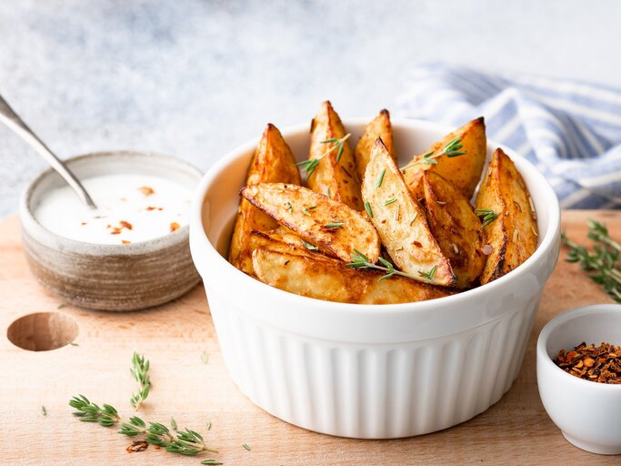 Kohlrabi-Wedges mit Thymian in einer weißen Schale auf einem Brett, darauf außerdem eine Schale Dip und eine Schale mit getrockneten Gewürzen.  | © adobe Stock/ CHZU