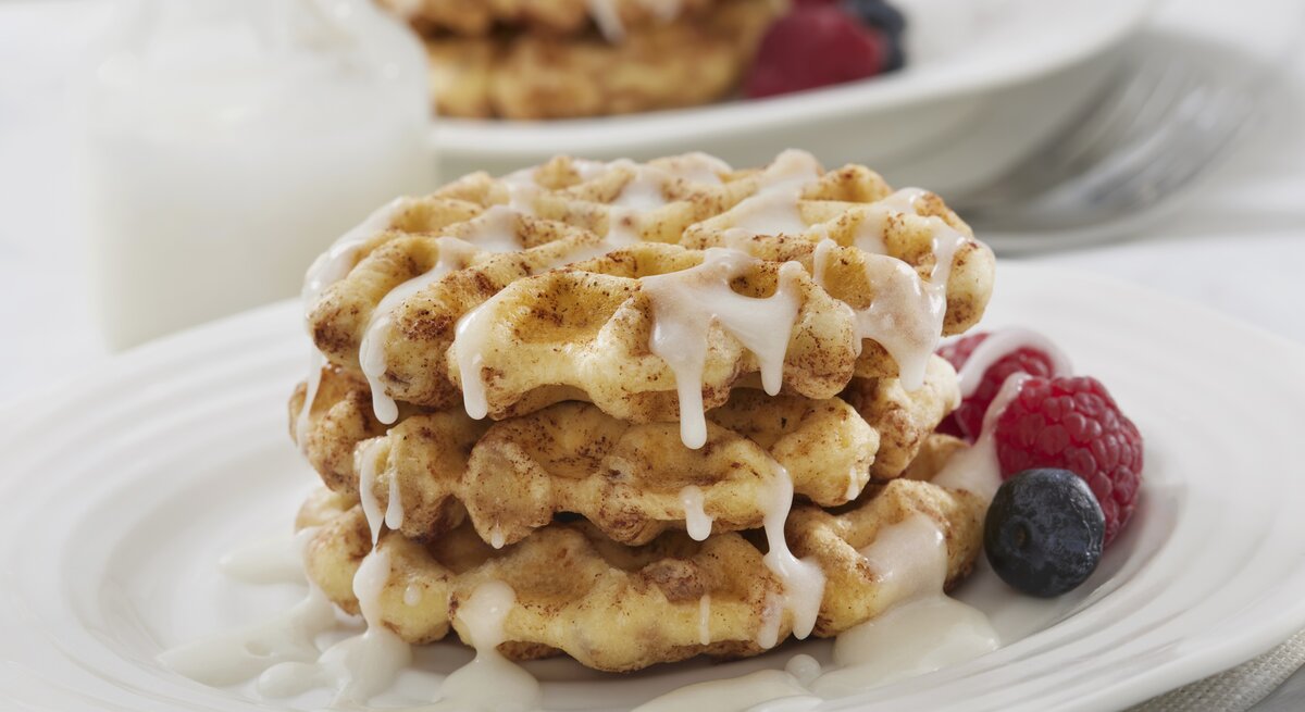 Drei Zimtschnecken-Waffeln mit Zuckerguss und Früchten auf weißem Teller. 