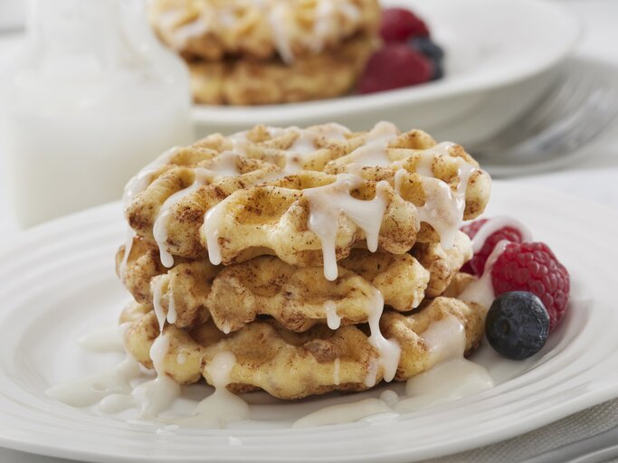 Drei Zimtschnecken-Waffeln mit Zuckerguss und Früchten auf weißem Teller.  | © Getty Images/LauriPatterson