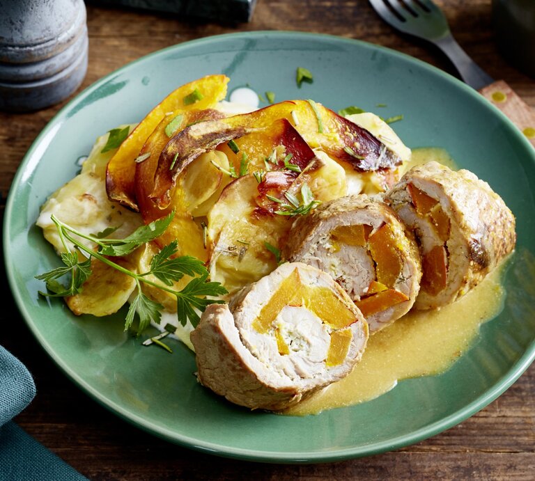 Schnitzelröllchen mit Kürbisgratin auf einem grauen Teller; auf dem Holzuntergrund ist eine Gabel, ein Tuch und eine Gewürzmühle.  | © EAT CLUB / Isabell Triemer 