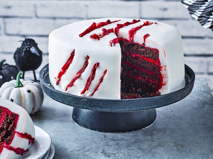 Auf einem Tortenteller steht eine gruselige Halloween-Torte. Sie ist mit weißem Fondant eingedeckt und hat blutige Risse als Dekoration. | © StockFood / Immediate Media / Good Food