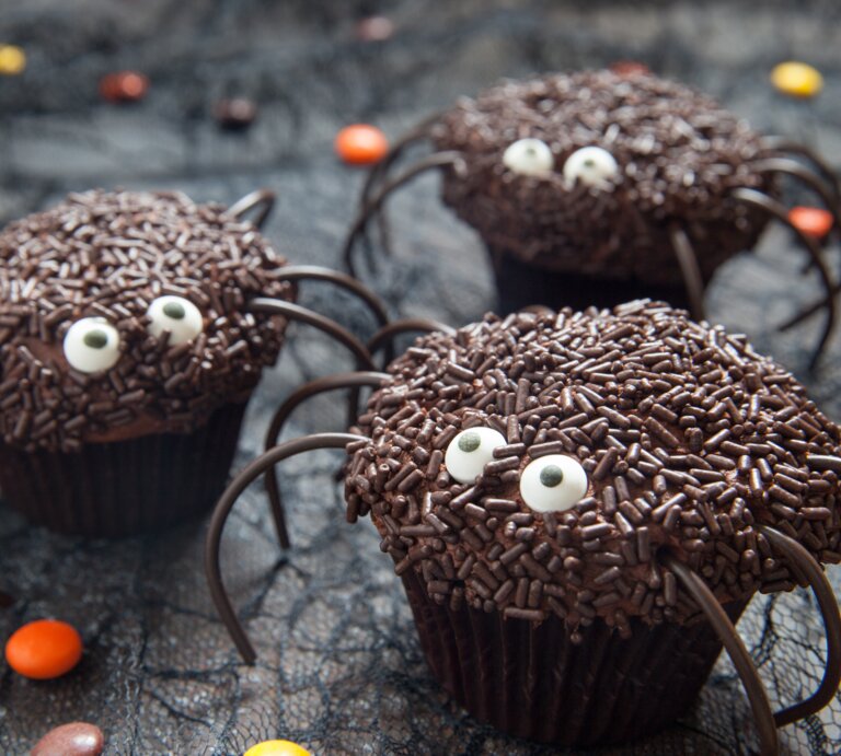 Süße Spinnen-Muffins mit Halloween auf dunklem Untergrund. Daneben liegen Schokolinsen in verschiedenen Farben.  | © Adobe Stock/azurita