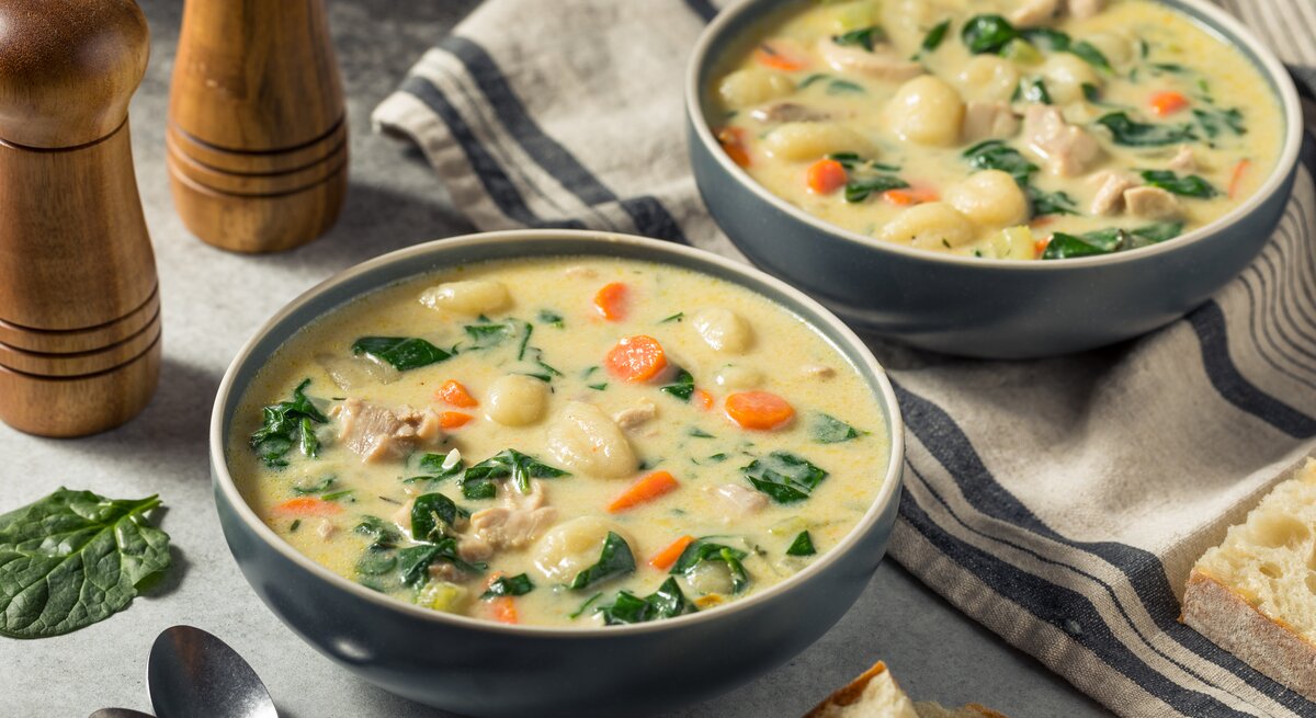 Zwei Portionen reichhaltige Suppe mit Huhn, Gemüseeinlage und Brotstück, rustikal serviert.