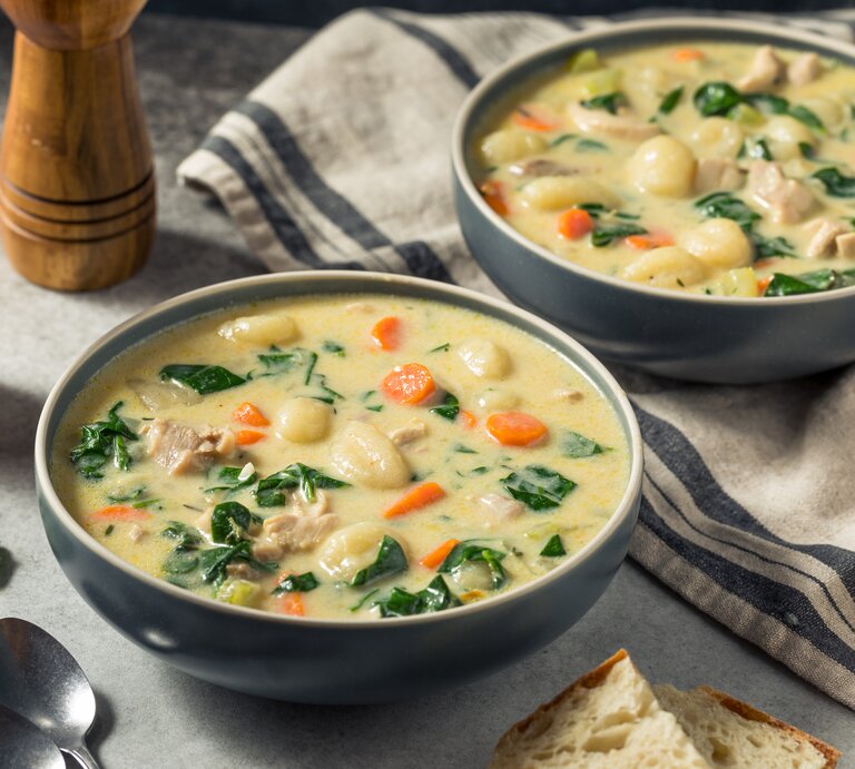 Zwei Portionen reichhaltige Suppe mit Huhn, Gemüseeinlage und Brotstück, rustikal serviert. | © Getty Images/bhofack2