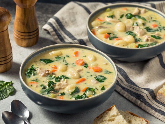 Zwei Portionen reichhaltige Suppe mit Huhn, Gemüseeinlage und Brotstück, rustikal serviert. | © Getty Images/bhofack2