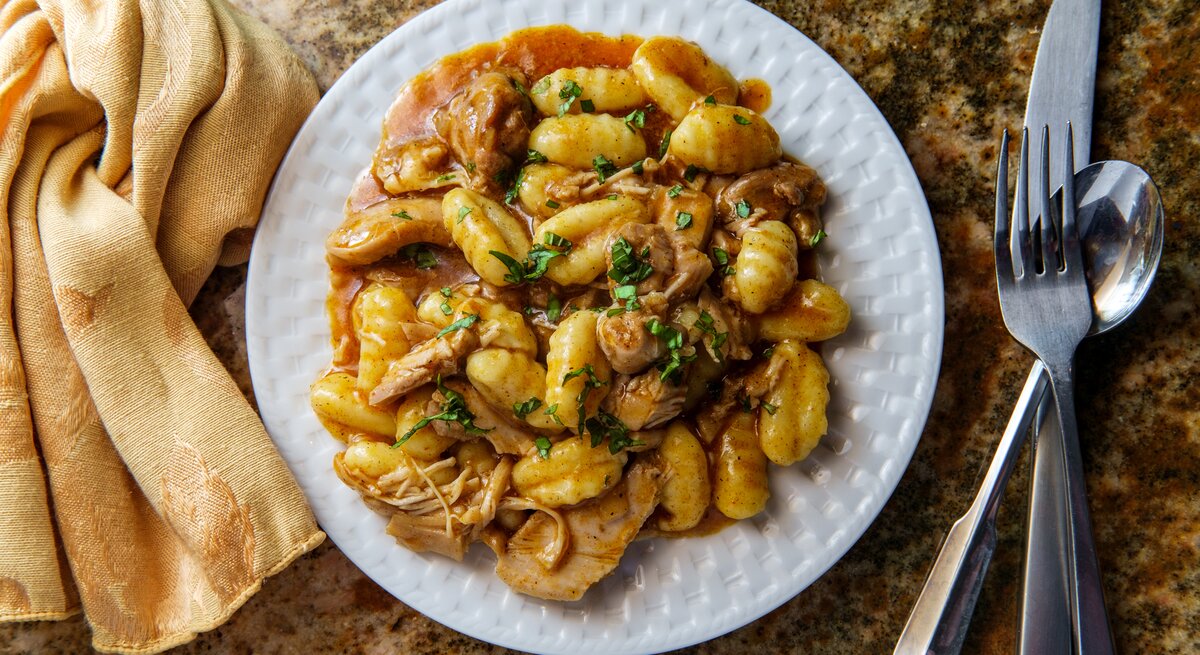 Gnocchi mit Gulasch auf weißem Teller, angerichtet auf Marmoruntergrund.
