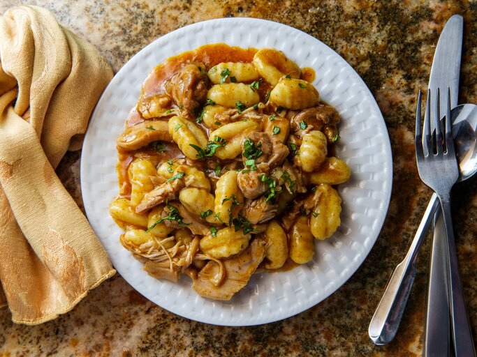 Gnocchi mit Gulasch auf weißem Teller, angerichtet auf Marmoruntergrund. | © Getty Images/EzumeImages