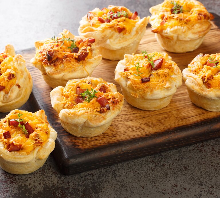 Blätterteig-Muffins mit Schinken & Käse auf Holzbrett.  | © Getty Images/ALLEKO