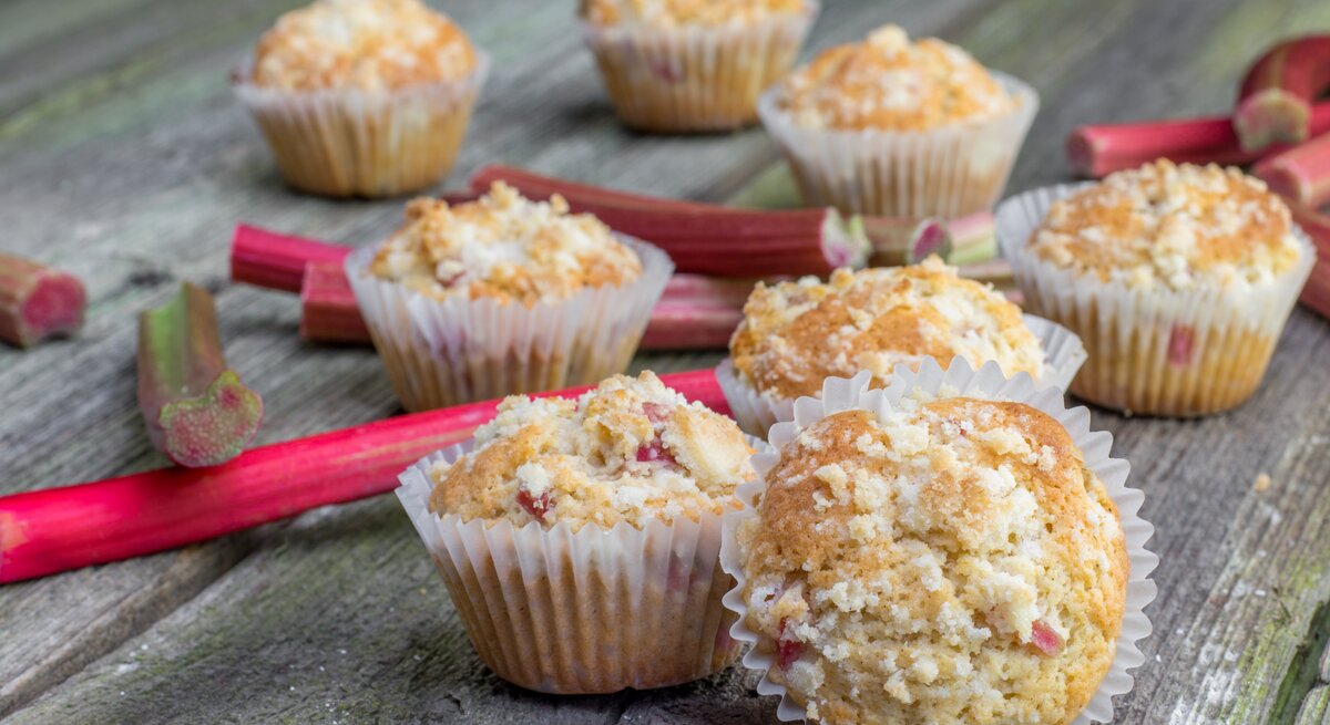 Mehrere Muffins auf einem Holztisch mit Rhabarberstangen.