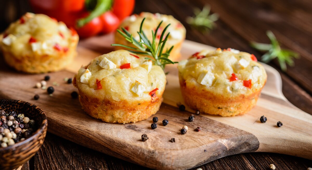 Feta-Muffins mit Paprika auf einem Holzschneidebrett neben einer Paprika