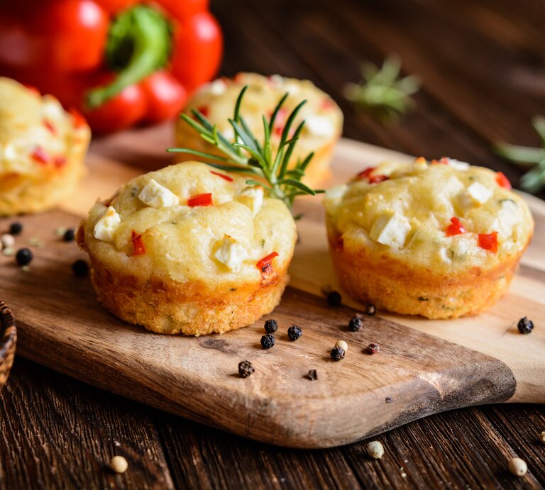 Feta-Muffins mit Paprika auf einem Holzschneidebrett neben einer Paprika | © Getty Images/NoirChocolate