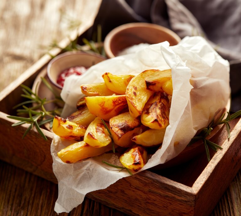 Eine Portion Kohlrabi-Pommes, eingewickelt in eine Papiertüte, auf einem Holztablett. Daneben Schälchen mit Dips. | © Adobe Stock/ zi3000