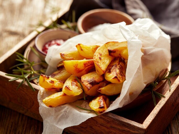 Eine Portion Kohlrabi-Pommes, eingewickelt in eine Papiertüte, auf einem Holztablett. Daneben Schälchen mit Dips. | © Adobe Stock/ zi3000