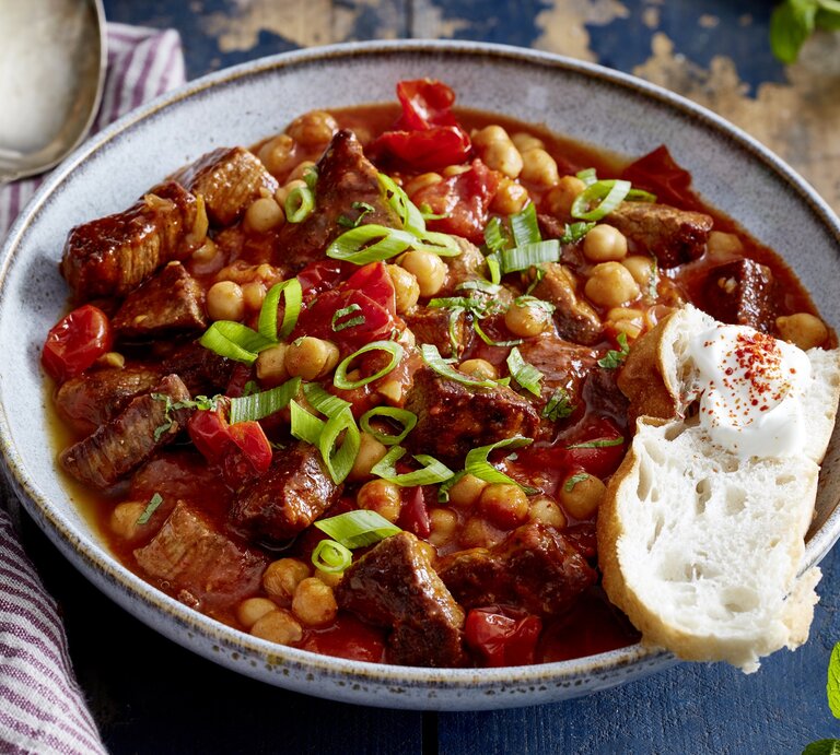 Ein großer Teller mit orientalischem Gulasch und Fladenbrot steht auf einem gemusterten Teller. Neben dem Teller liegt ein Löffel. | © Eat Club / Isabell Triemer