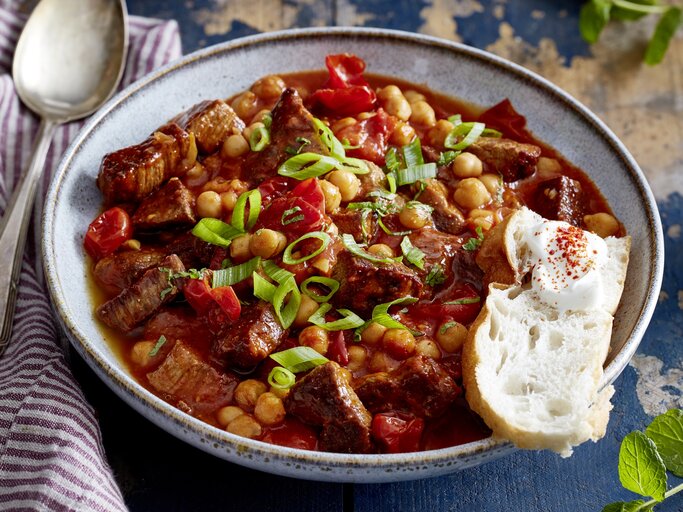 Ein großer Teller mit orientalischem Gulasch und Fladenbrot steht auf einem gemusterten Teller. Neben dem Teller liegt ein Löffel. | © Eat Club / Isabell Triemer
