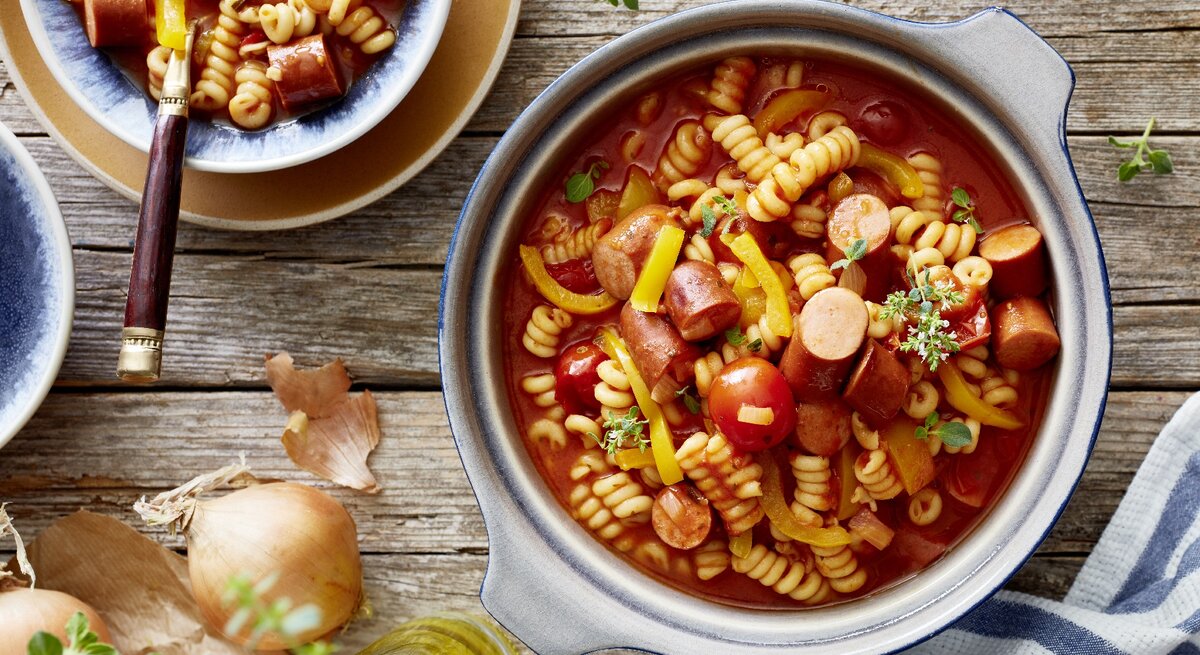 One-Pot-Wurstgulasch in Topf auf Holztisch. 