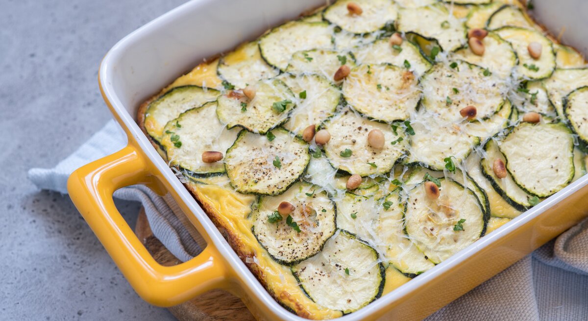 Zucchini-Auflauf mit Hackfleisch und Feta in gelber Auflaufform auf hellem Untergrund. 