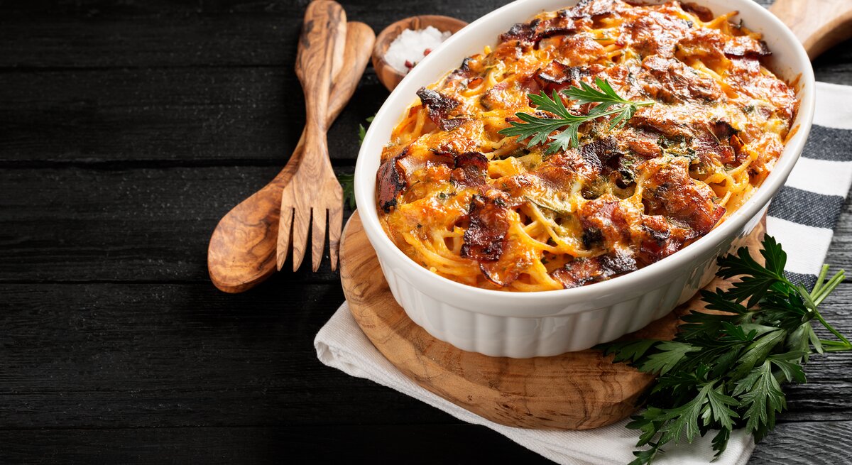 Spaghetti-Auflauf mit Hähnchen in einer weißen Auflaufform. Daneben eine Schale mit Meersalz und hölzernes Besteck. 