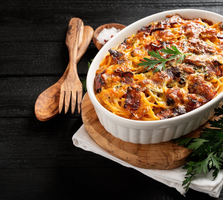 Spaghetti-Auflauf mit Hähnchen in einer weißen Auflaufform. Daneben eine Schale mit Meersalz und hölzernes Besteck.  | © Shutterstock/ nelea33