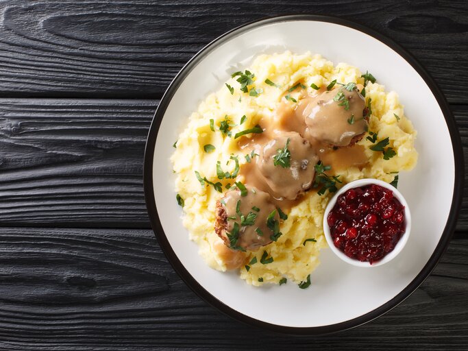 Von-Oben-Ansicht eines Tellers mit finnischen Hackbällchen, cremiger Soße und Kartoffelbrei. Daneben steht eine Schale Kompott.  | © Shutterstock/AS Foodstudio