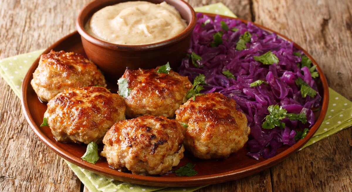Brauner Teller mit Frikadellen, Dip und Rotkohl auf Holztisch. 