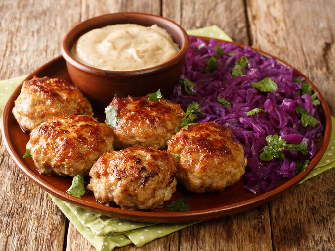 Brauner Teller mit Frikadellen, Dip und Rotkohl auf Holztisch.  | © Shutterstock/Sergii Koval