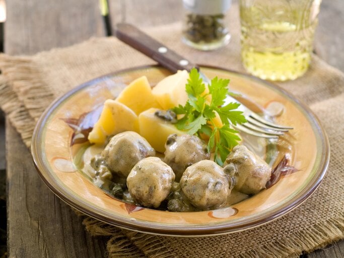 Königsberger Klopse mit Kapern und Soße zu Kartoffeln auf einem kitschigen Teller.  | © iStock/ Wiktory